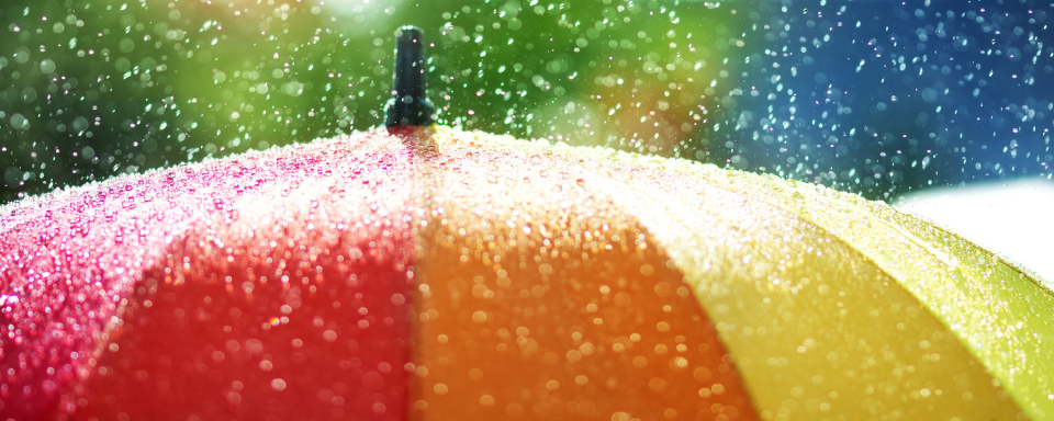 Rain falls on a rainbow-coloured umbrella.
