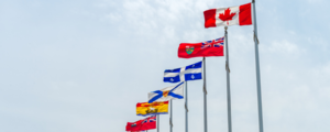 National and provincial flags of Canada displayed on flagpoles against an overcast sky.